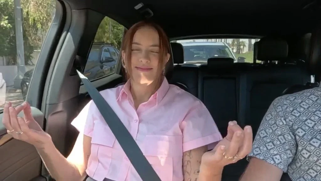 A woman in a pink shirt practices meditation in a car.