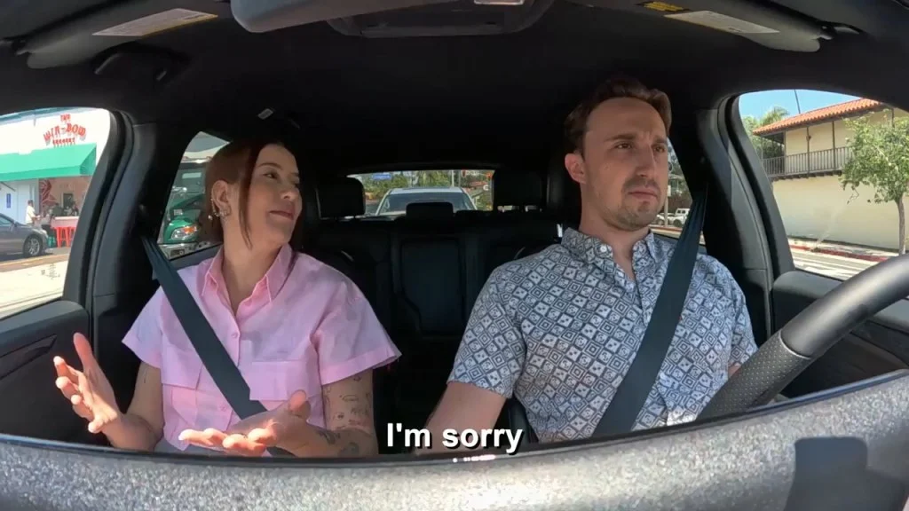 A man and a woman in a car, with the woman saying "I'm sorry."