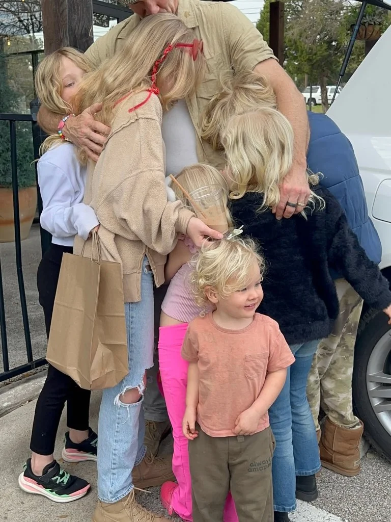 A family, consisting of a man and several blonde-haired children, embrace each other.