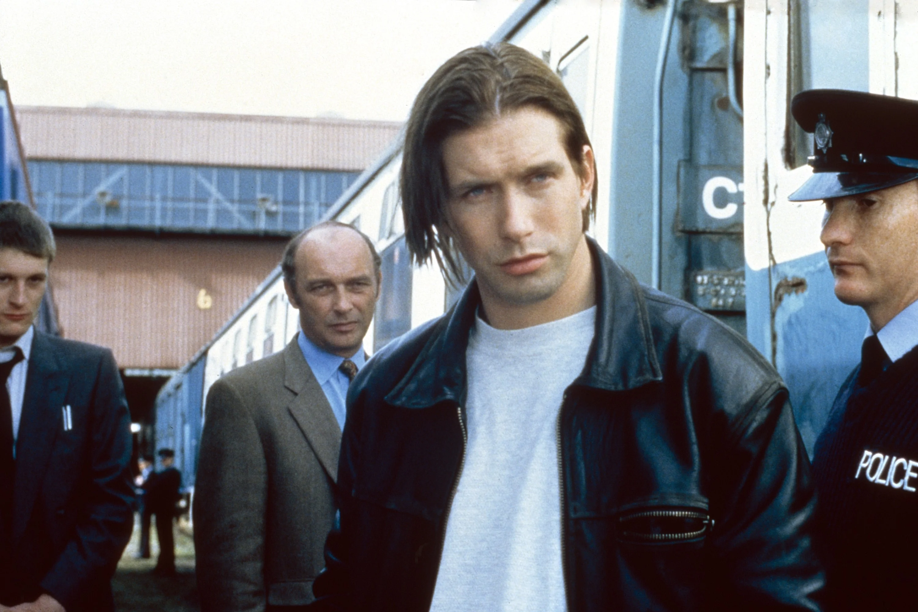 Stephen Baldwin in a leather jacket and t-shirt, next to a police officer and two men in suits, in a scene from the film Crimetime.