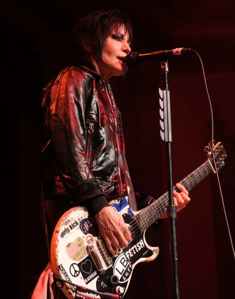 Joan Jett performing on stage with her guitar and a microphone.