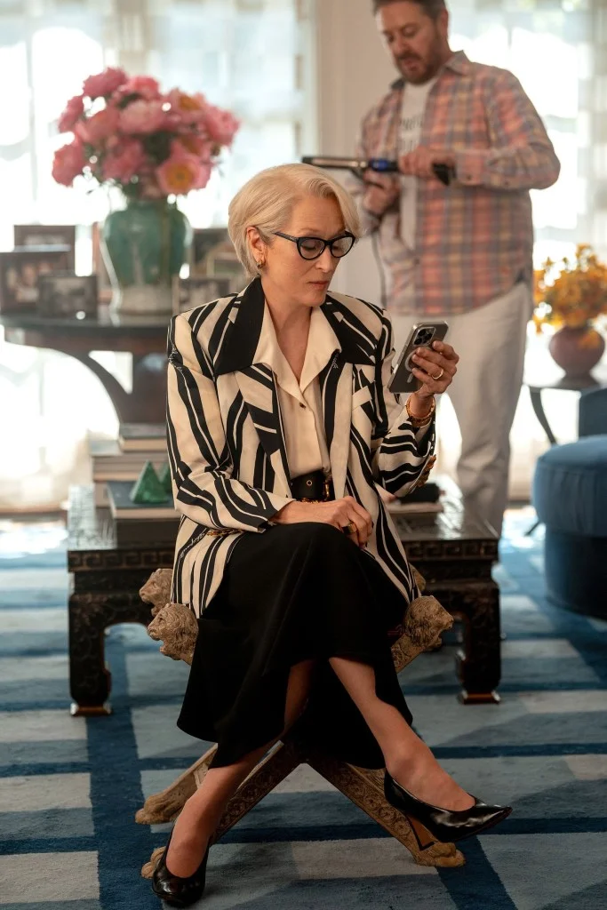 Woman in a black and white striped blazer looking at her phone.