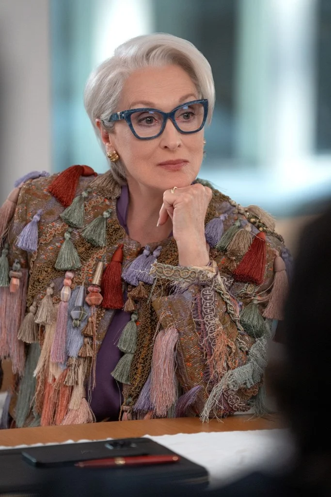 Meryl Streep as Miranda Priestly in a colorful tassel jacket and blue glasses.