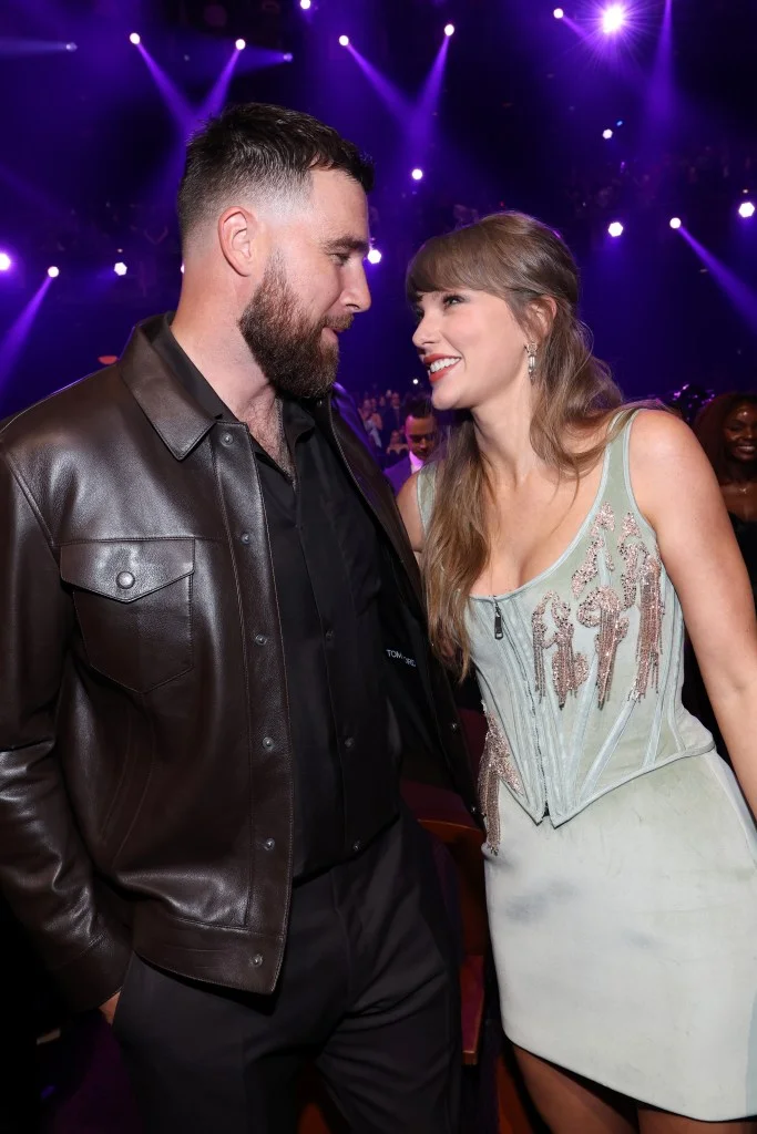 Travis Kelce and Taylor Swift smiling at each other at an awards show.