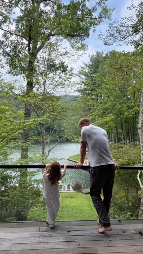 Prince Harry and Princess Lilibet looking out over a lake from a balcony.