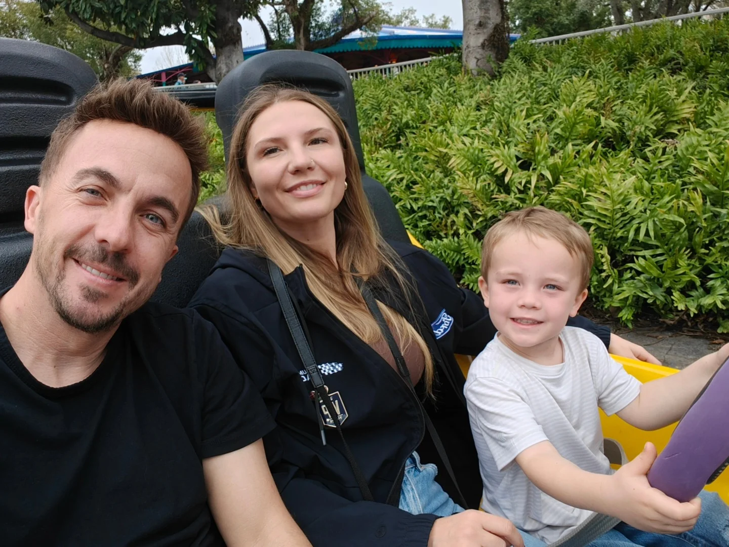 Frankie Muniz, his wife, and their son sitting in a ride vehicle.