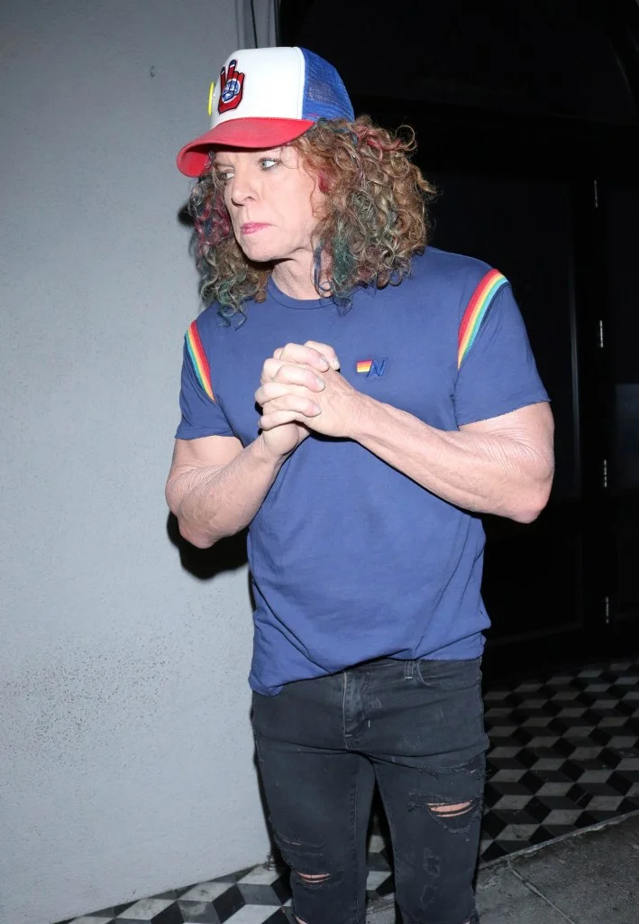 Carrot Top in Los Angeles, wearing a blue shirt with rainbow stripes on the sleeves, ripped black jeans, and a red, white, and blue trucker hat.
