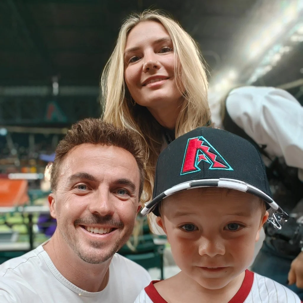 Frankie Muniz, his wife Paige Price, and their son, all smiling at a baseball game.