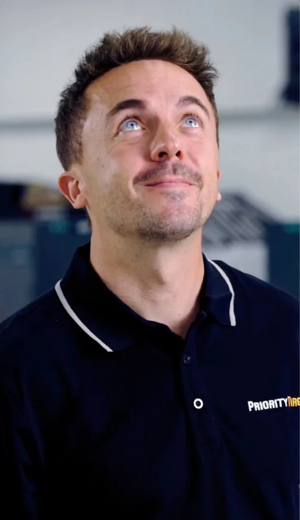 Man in a black Priority Tire polo shirt looking up with blue eyes.