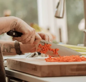 hands using a knife to chop carrots on a counter.