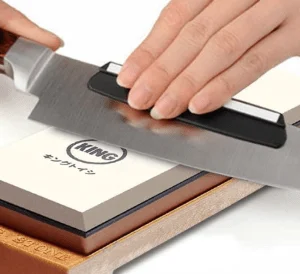 hands holding a knife being sharpened on a whetstone.