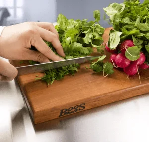hand cutting radishes on a cutting board.